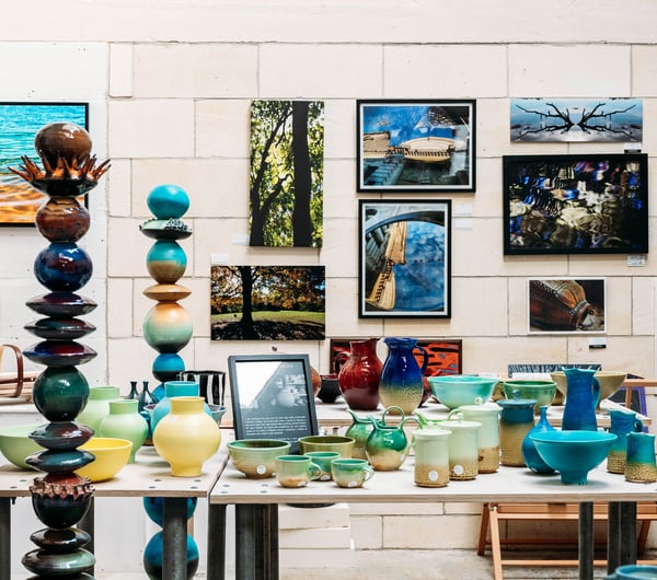 Unique sculptures and ceramics on table in front of a wall filled with artistic photography at Crafted Gallery in Ōamaru