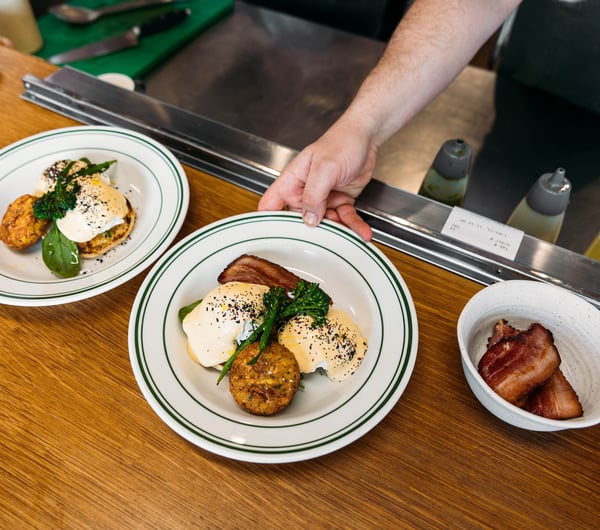 An outstretched arm places a plate of bacon and eggs and hollandaise on the pass at Cream Eatery in Hamilton.
