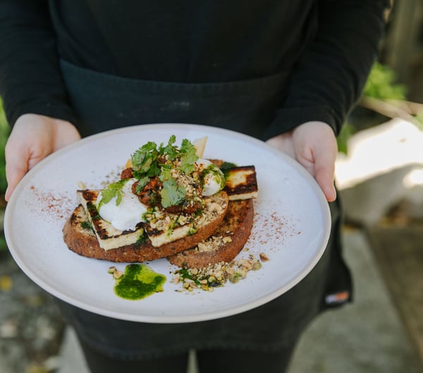 Person holding a plate of halloumi and poached eggs from Deville, Nelson.