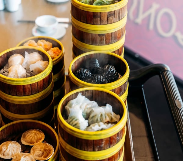 Stacks of bamboo steamer baskets with different types of dumplings inside each.
