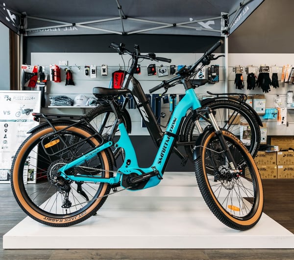 An electric blue e-bike displayed on a low white plinth inside Electrify.