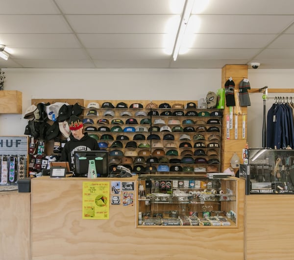 A man working behind the counter at Embassy where lots of caps are displayed on shelves.