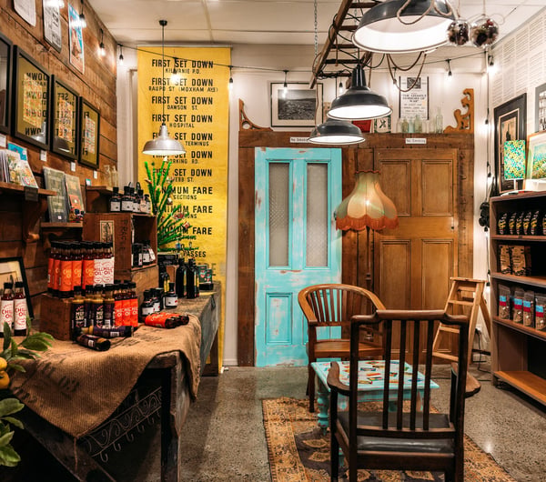 Interior of an artisan food shop with chilli oil on shelves, retro lampshades and antique chairs and table