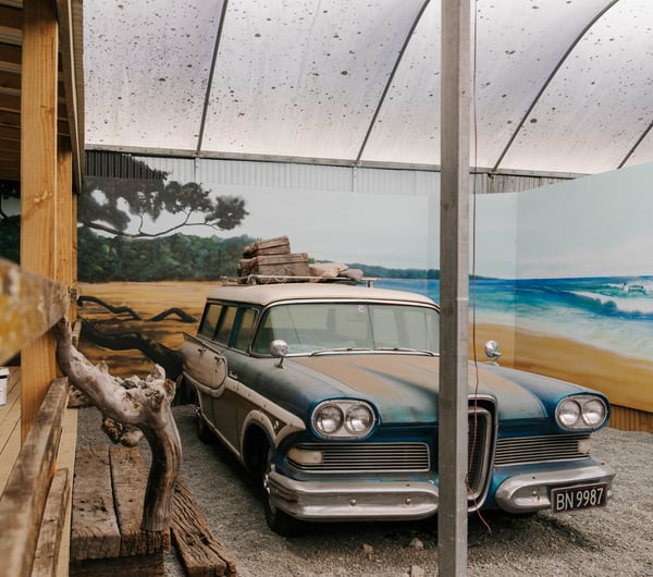 Classic car parked with a painted beach mural behind.