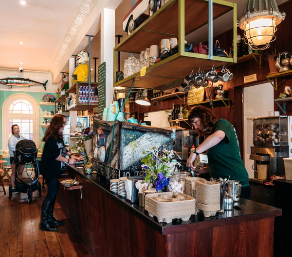 Barista making coffee behind cafe counter and cabinet