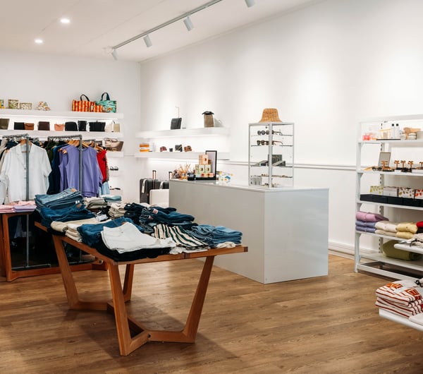 Contemporary fashion boutique with white shop counter surrounded by clothing on metal racks and jeans folded on timber tables