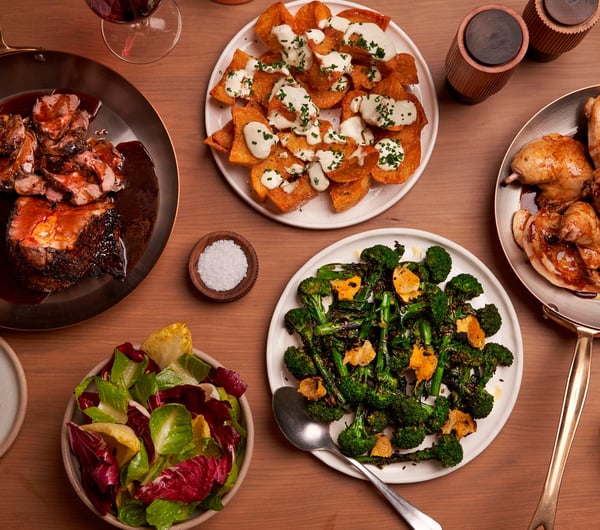 A flatlay of plates of meat and vegetables on a table.