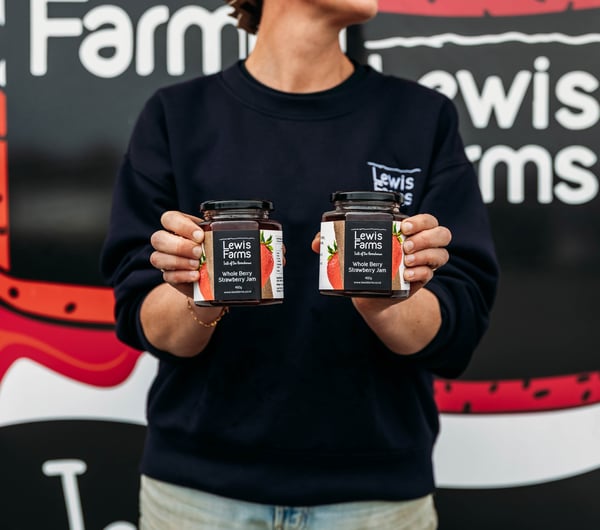 Staff member holding two jars of preserves at Lewis Farms.