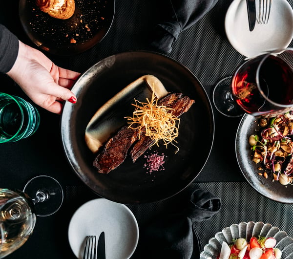Staff member places a food dish down on the table with wine glasses and other plates.