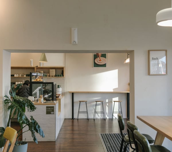 Interior of NOKI in Christchurch with wooden furnishings, green leather chairs, white-tiled countertop and framed art prints including someone sticking their finger in a fried egg