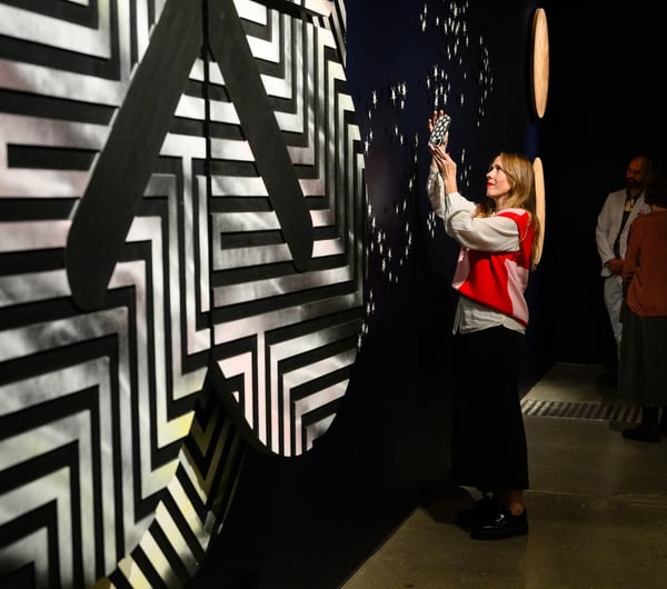 Woman looking at an exhibition and taking a photo of it at Pātaka Art + Museum.