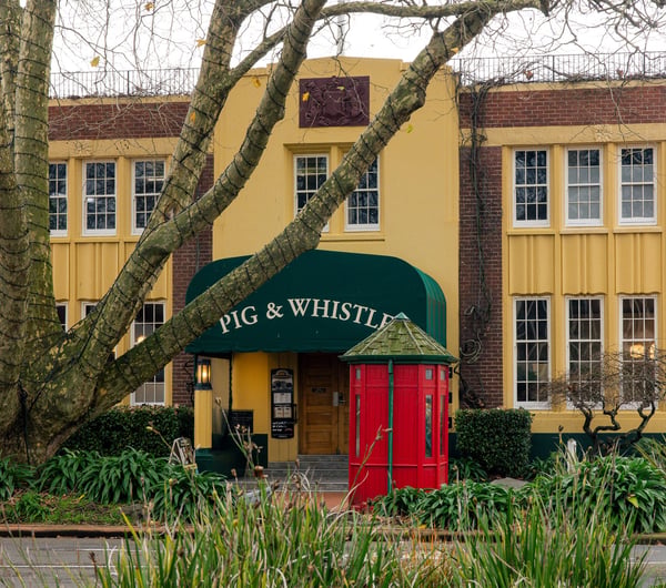 Outside of the Pig & Whistle heritage building with a red telephone box and large tree.