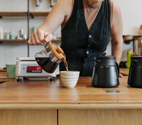 A woman pouring black coffee into a cup.