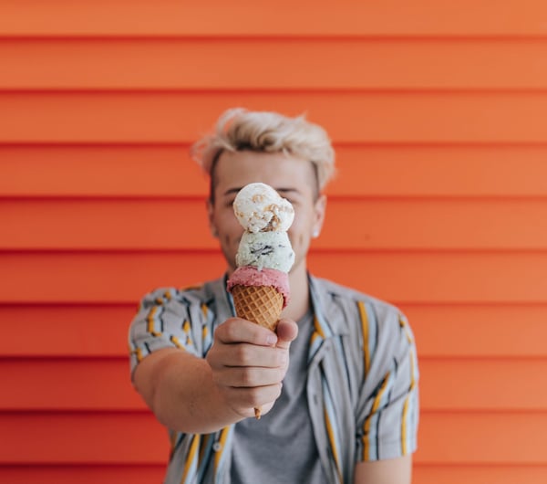 Double scoop gelato on a cone in front of an orange wall.