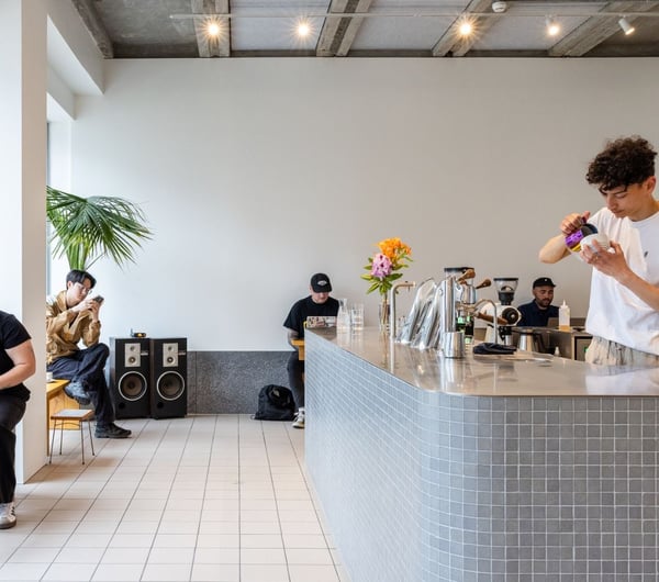 Modern cafe space with barista behind counter making a coffee and customers sitting at tables, in Rook.