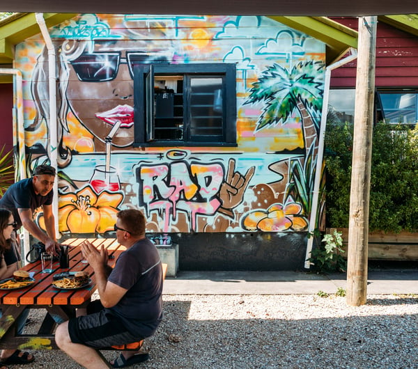 Customers sitting at a picnic table outside Roots Bar on a sunny day.
