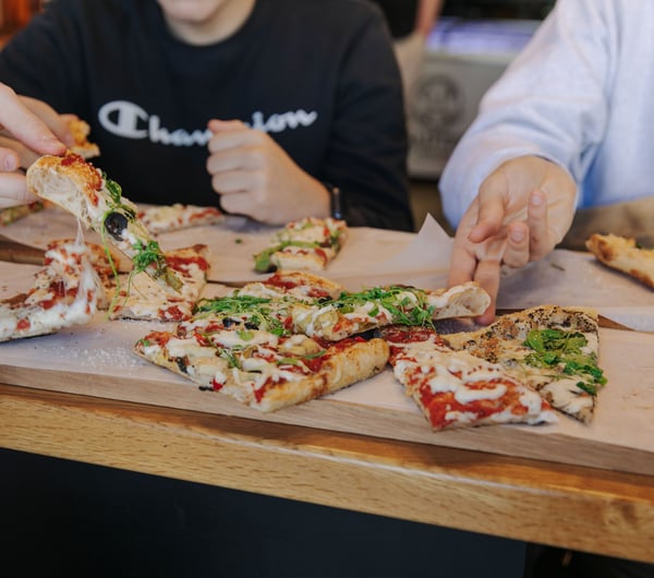 People sitting around a table with a pizza in the middle all sharing.