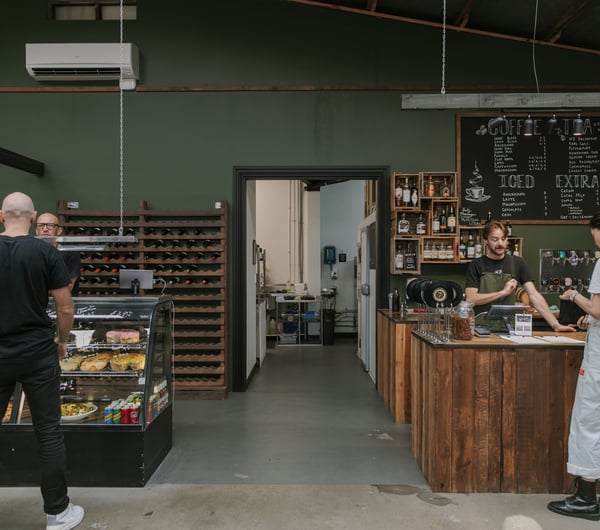 Customers standing around at a counter inside a green decorated cafe.