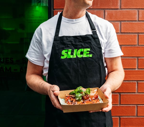 Pizza assistant holding a slice of pizza outside Slice.