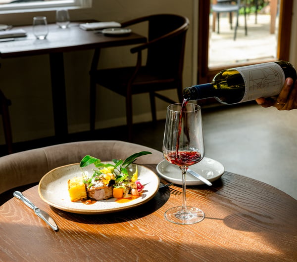Waiter pouring glass of red wine next to a refined plate of food