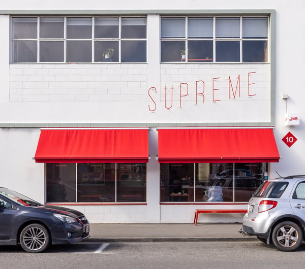 White brick exterior of cafe Supreme Supreme, with bright red awning.