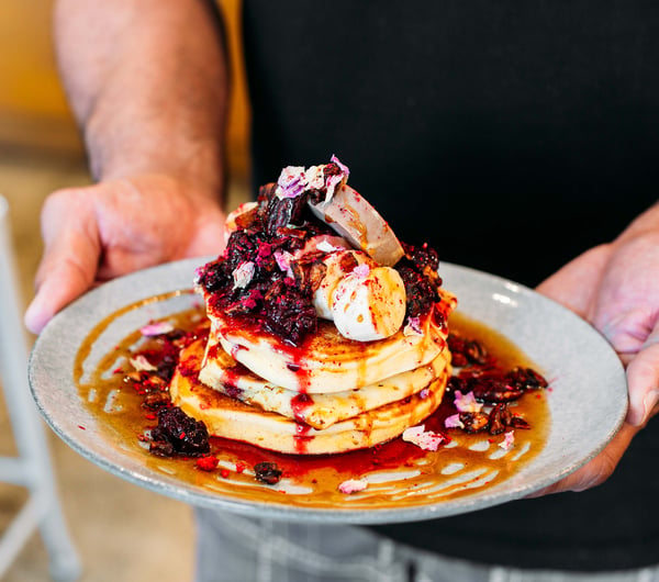 Man holding a plate of hotcakes with berries from t bay cafe, Porirua.