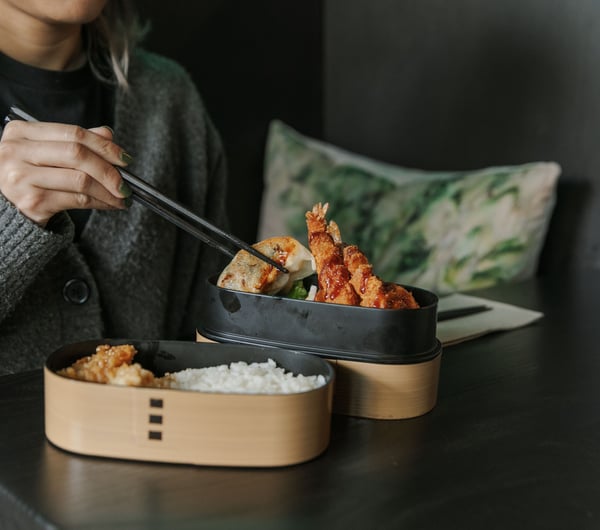 Hands holding chopsticks reaching for food on a plate.