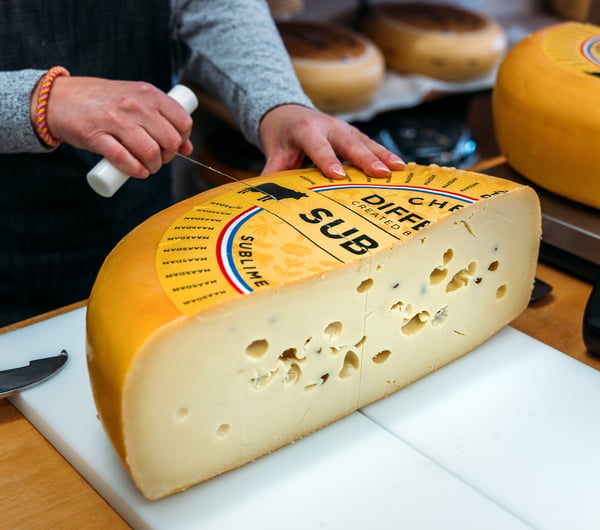 Someone slicing a wheel of Dutch cheese in specialty food store