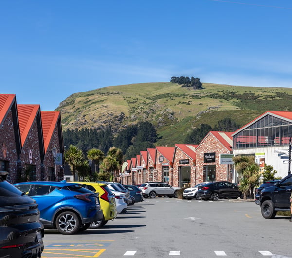 The outside of the red bricked buildings on a bright sunny day, with cars in the car park and a hill in the background at The Tannery.