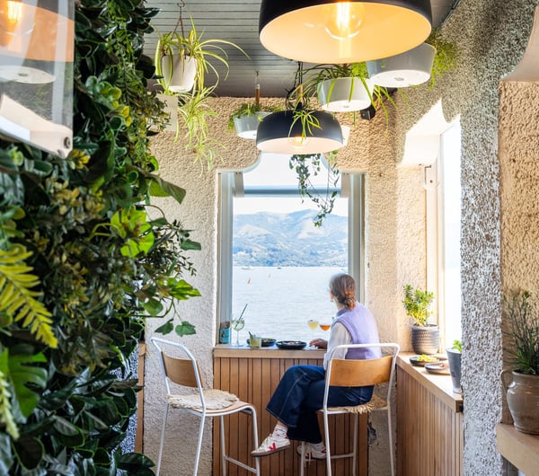 Woman sitting next to window at Tini bar with food and cocktails looking out on to waterfront views