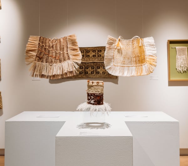 Weaved bags and mats on display inside a gallery.