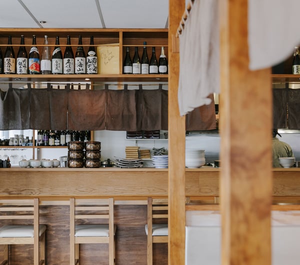 Looking over the counter into the kitchen where the chef is.