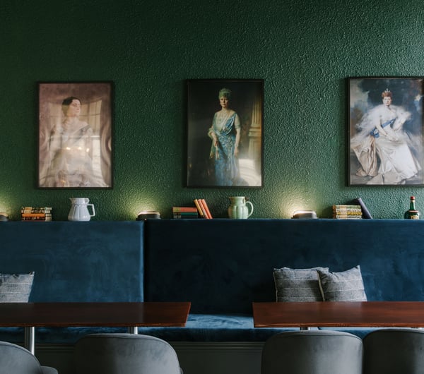 Plush blue seating set against a dark green wall filled with portraits of queens