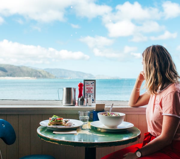 Customer sitting at an outdoor table at Maranui Cafe with the sea behind her.