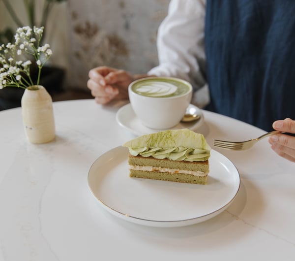 Person sitting at table at Sweet Soul Patisserie with a cup of matcha latte and a beautiful matcha flavoured patisserie
