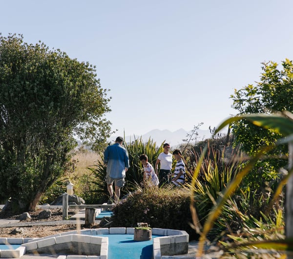 Kids playing mini golf with their parents on a sunny day.
