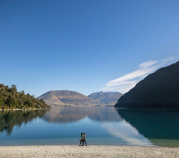 Two people walking along a lake on a sunny day.