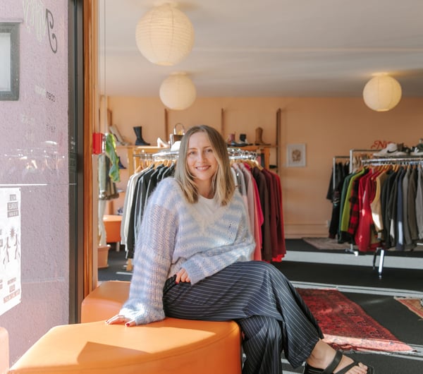 Photo of Rosie Carroll sitting on orange semi-circle couch at her secondshop Nifty in Christchurch