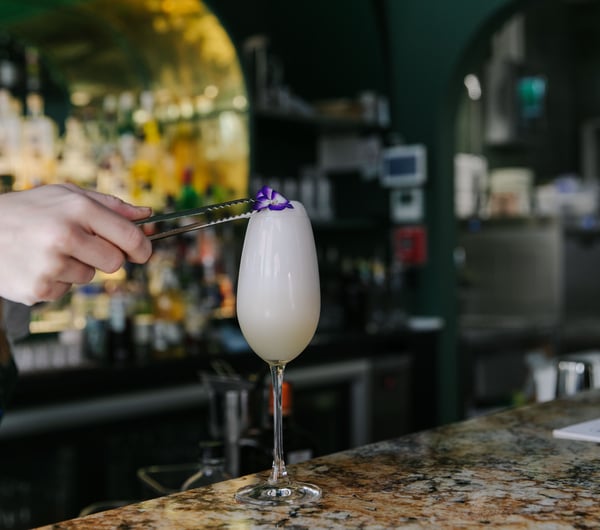 Bartender adding purple pansy as a garnish on top of a cocktail