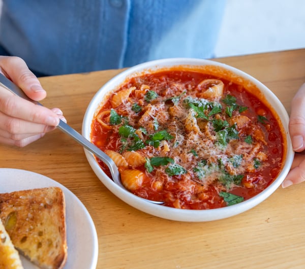 Close up of someone dipping spoon into minestrone soup from Estelle next to plate of toast