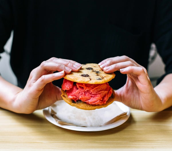 Two hands holding an ice cream cookie sandwich.