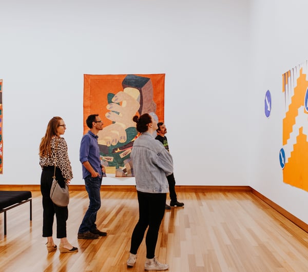 A group of adults looking intently at a colourful painting on a wall at Christchurch Art Gallery.