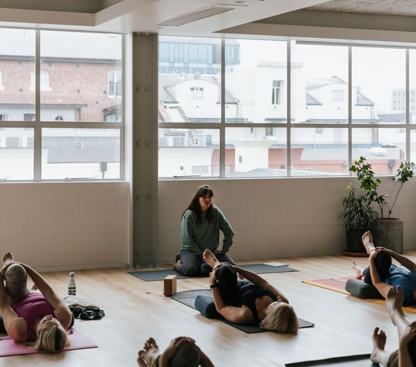 A yoga teacher taking a class of students lying on their backs.