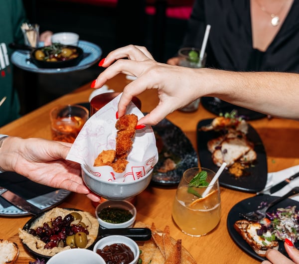 A hand reaching for a piece of fried chicken.