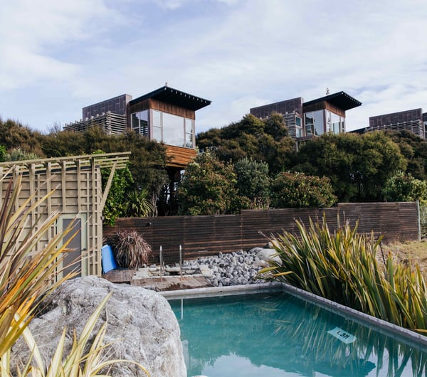 Wooden apartments set behind a swimming pool on a sunny day.