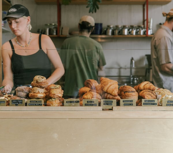 Three staff members behind the counter at Grizzly, with a cabinet filled with croissants, morning buns and filled bagels