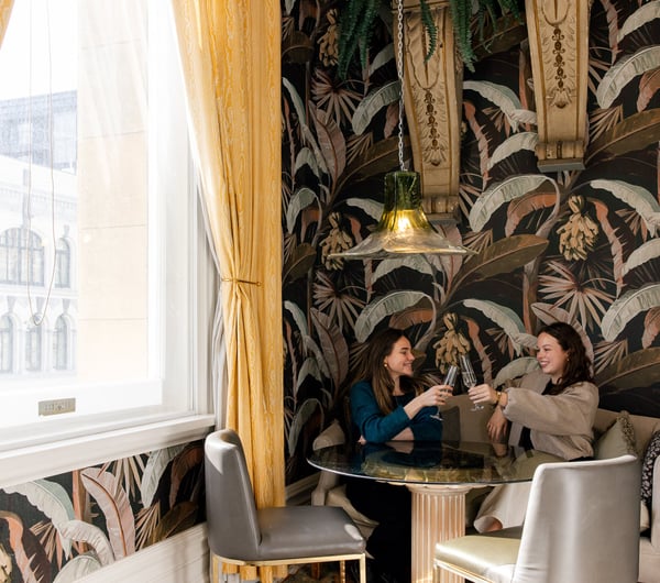 Two women toasting their wine glasses sitting at a table.