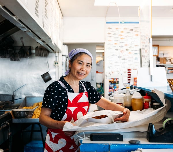 A woman packing fish and chips in a fish and chip shop.