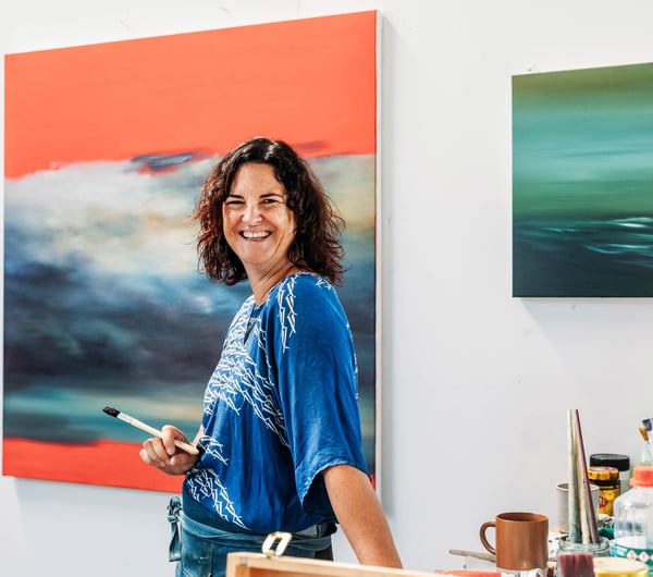 A woman holding a paint brush and smiling to camera.