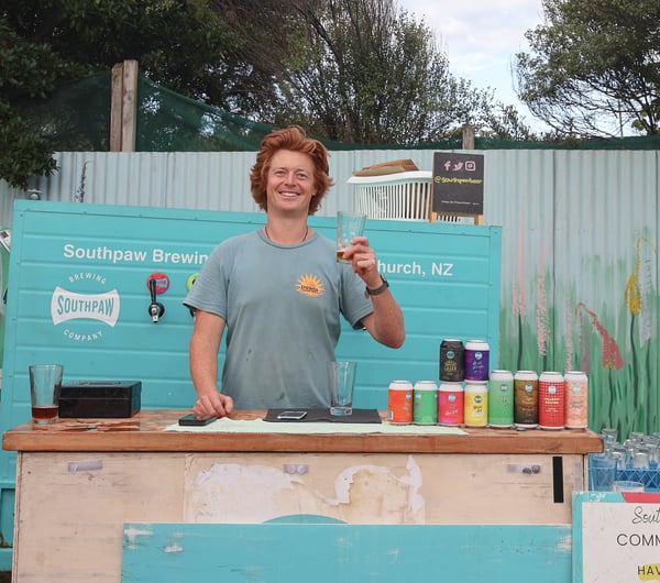 A man holding a beer and smiling to camera outside.